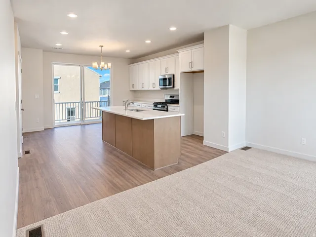 Bright open-concept living space with wood-finish flooring, a kitchen island, white cabinetry, and stainless steel appliances