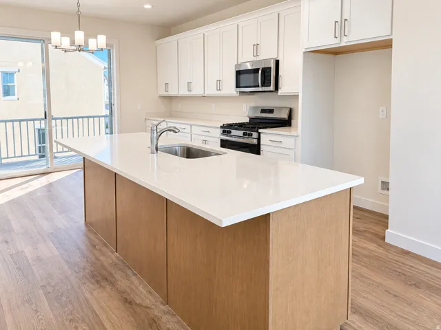 Kitchen featuring wood-finish flooring, white cabinetry, a large center island with a sink, stainless steel appliances, and a sliding glass door to a balcony