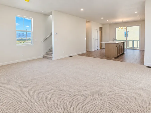 Open-concept living space featuring neutral carpeting, wood-finish flooring, a kitchen island with storage, and sliding glass door access to an outdoor area