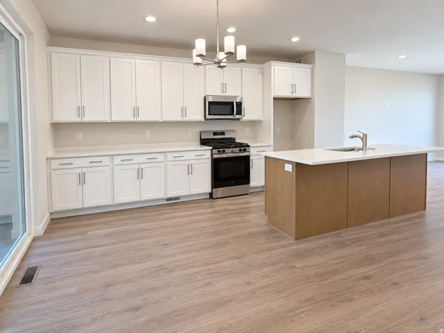 Kitchen featuring an island with an integrated sink, stainless steel appliances, white cabinetry, recessed lighting, and wood-finish flooring