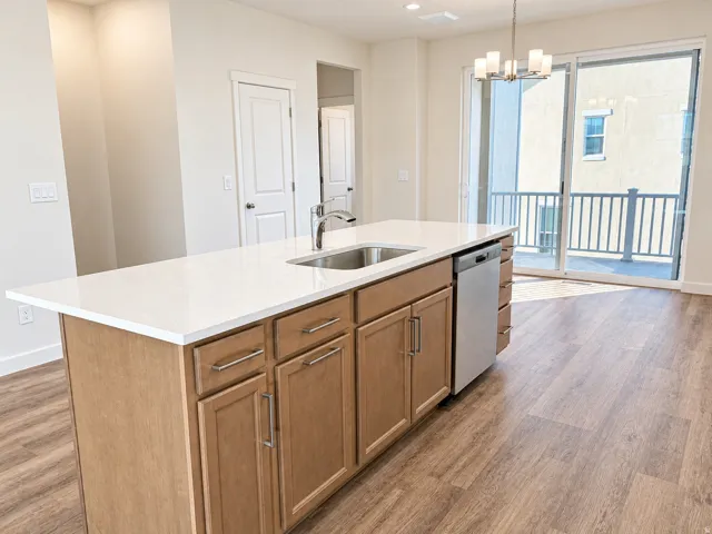 Kitchen island with a white countertop, undermount stainless steel sink, and light wood cabinetry