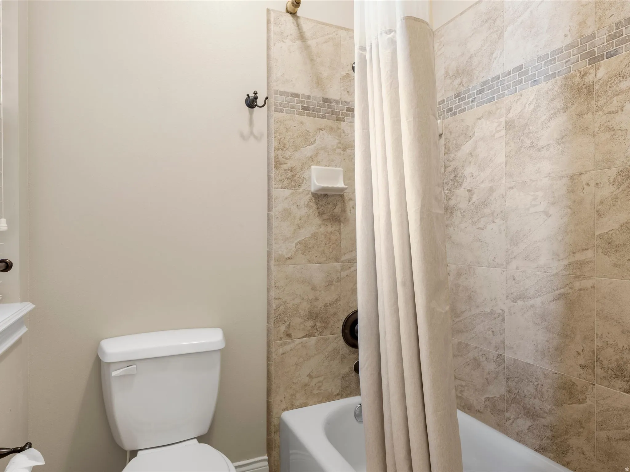 Bathroom with a tub/shower combination, extensive tile surround, and a decorative mosaic tile accent band