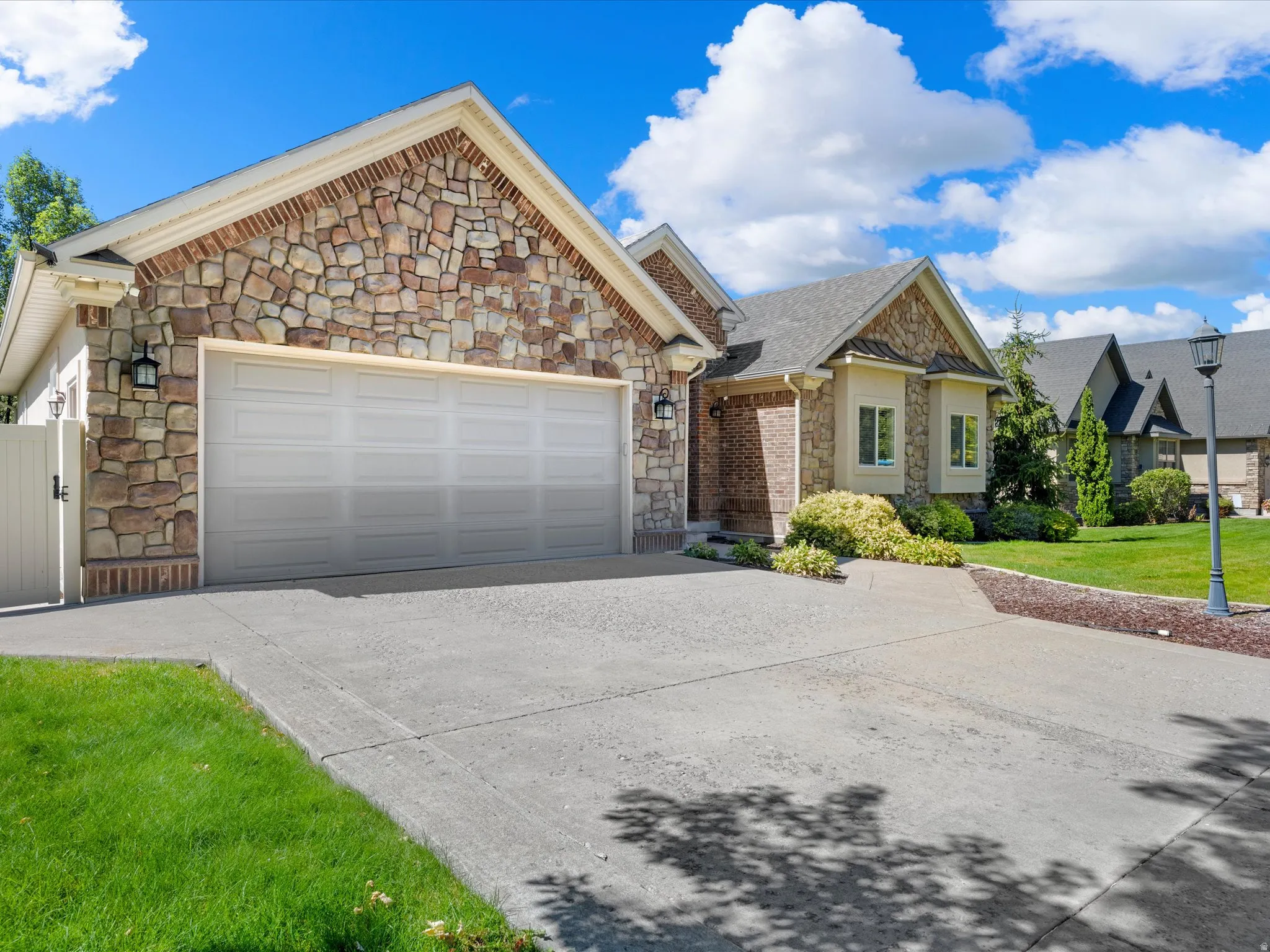 Stone veneer facade with brick accents, attached garage, concrete driveway, bay window, and manicured landscaping