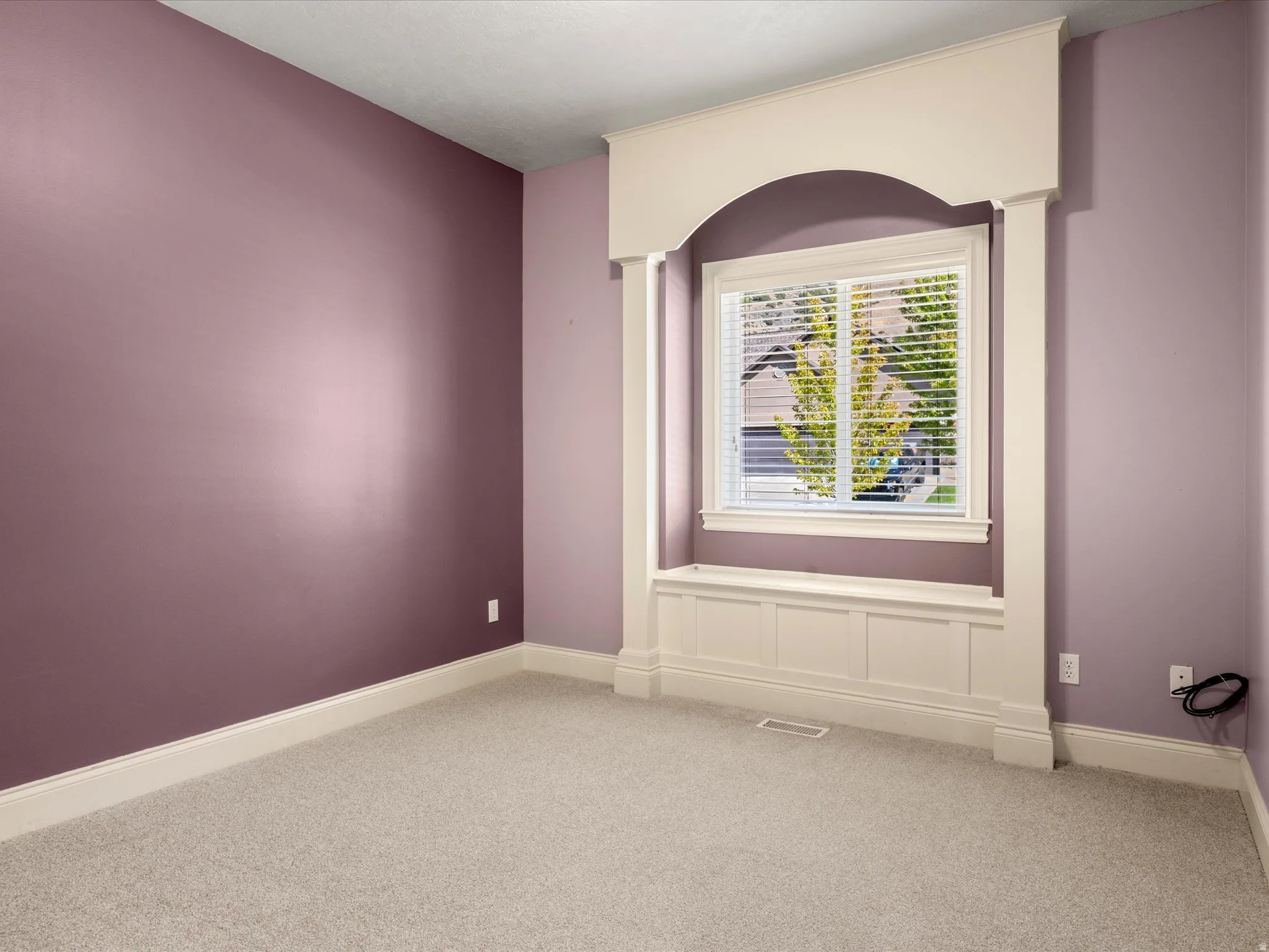 Window alcove with an arched architectural detail, integrated window seat with paneling, and neutral carpet flooring