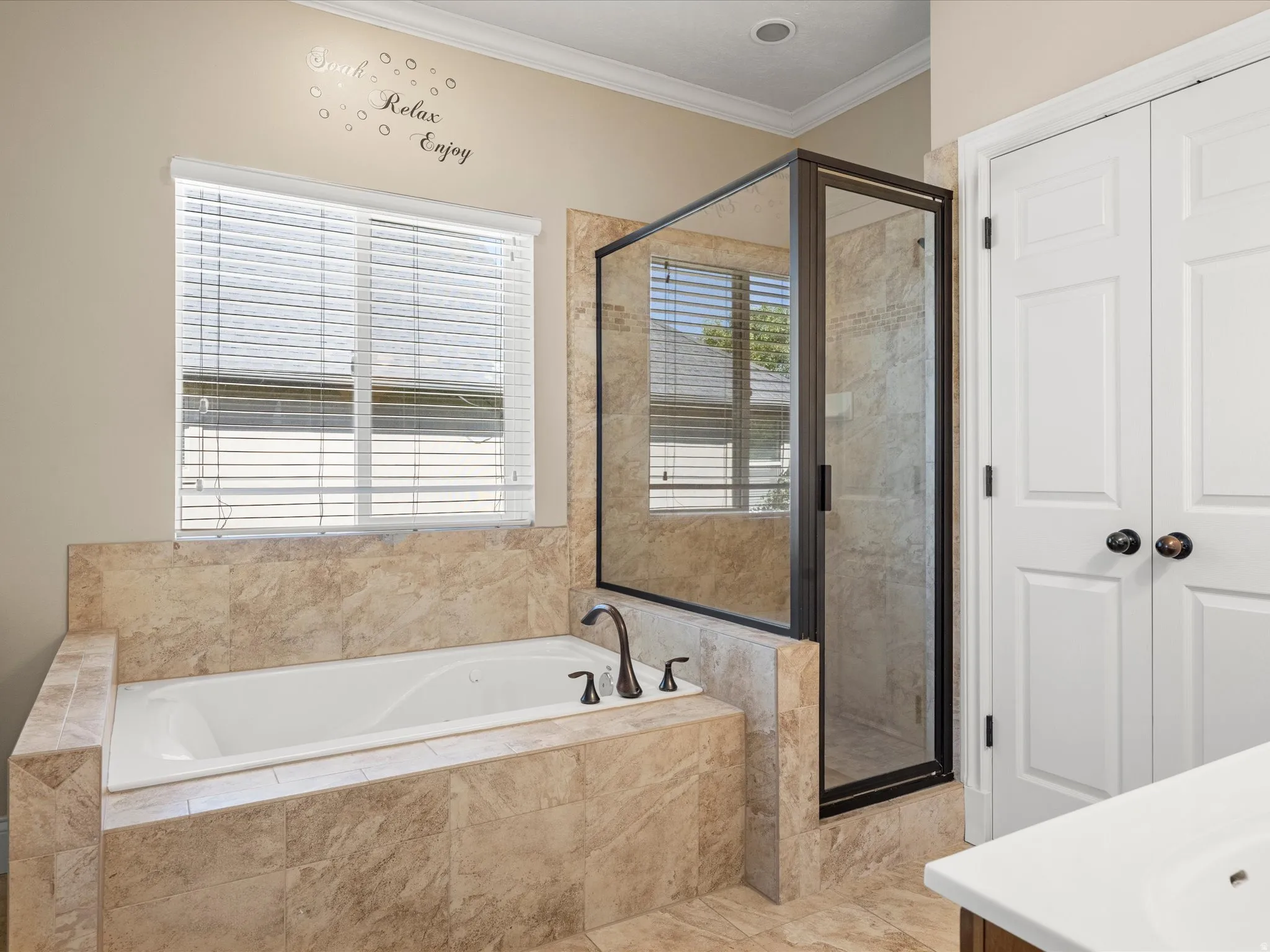 Built-in soaking tub with a dark bronze faucet, tile surround, and an adjacent glass-enclosed shower