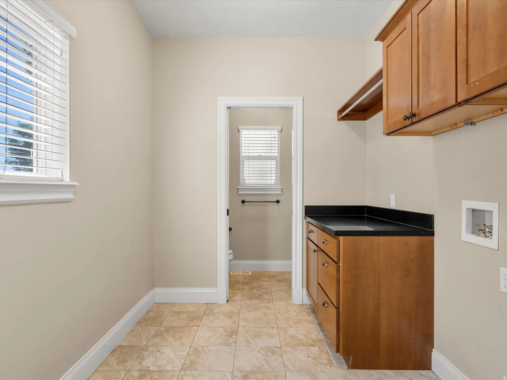 Utility space with wood-finish cabinetry, dark countertop, and tiled flooring