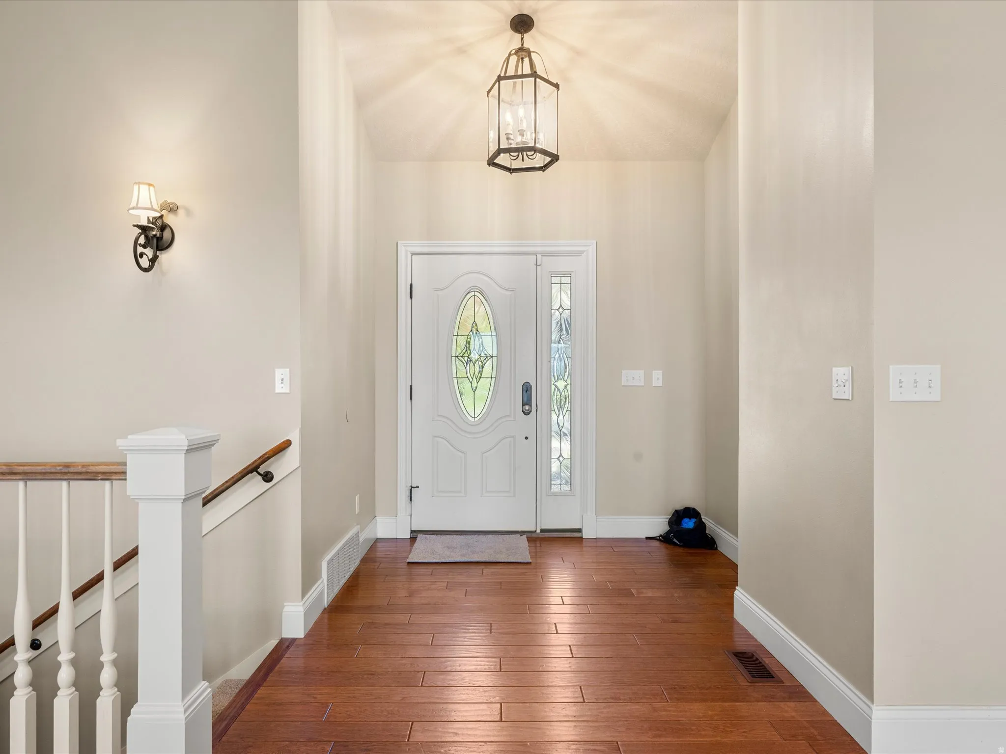 White paneled door with decorative oval glass insert, wood-finish flooring, white painted baseboards, and a wrought iron style wall sconce