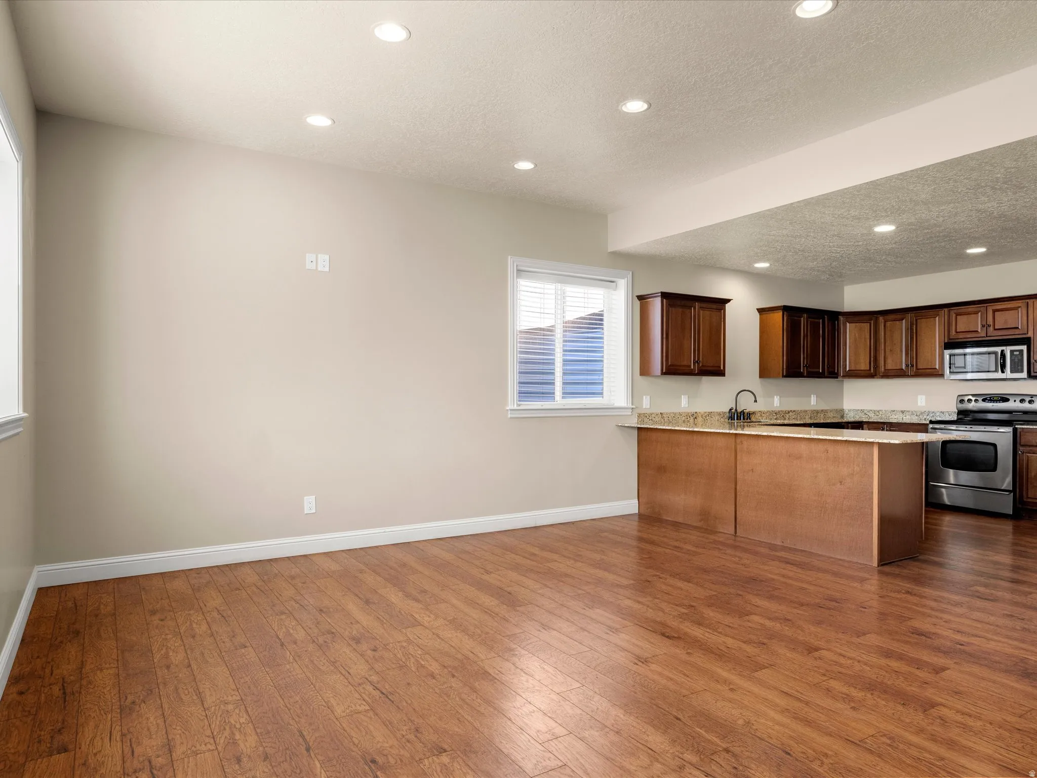 Wood-finish flooring, recessed lighting, and kitchen featuring wood cabinetry, stone countertops, and stainless steel appliances