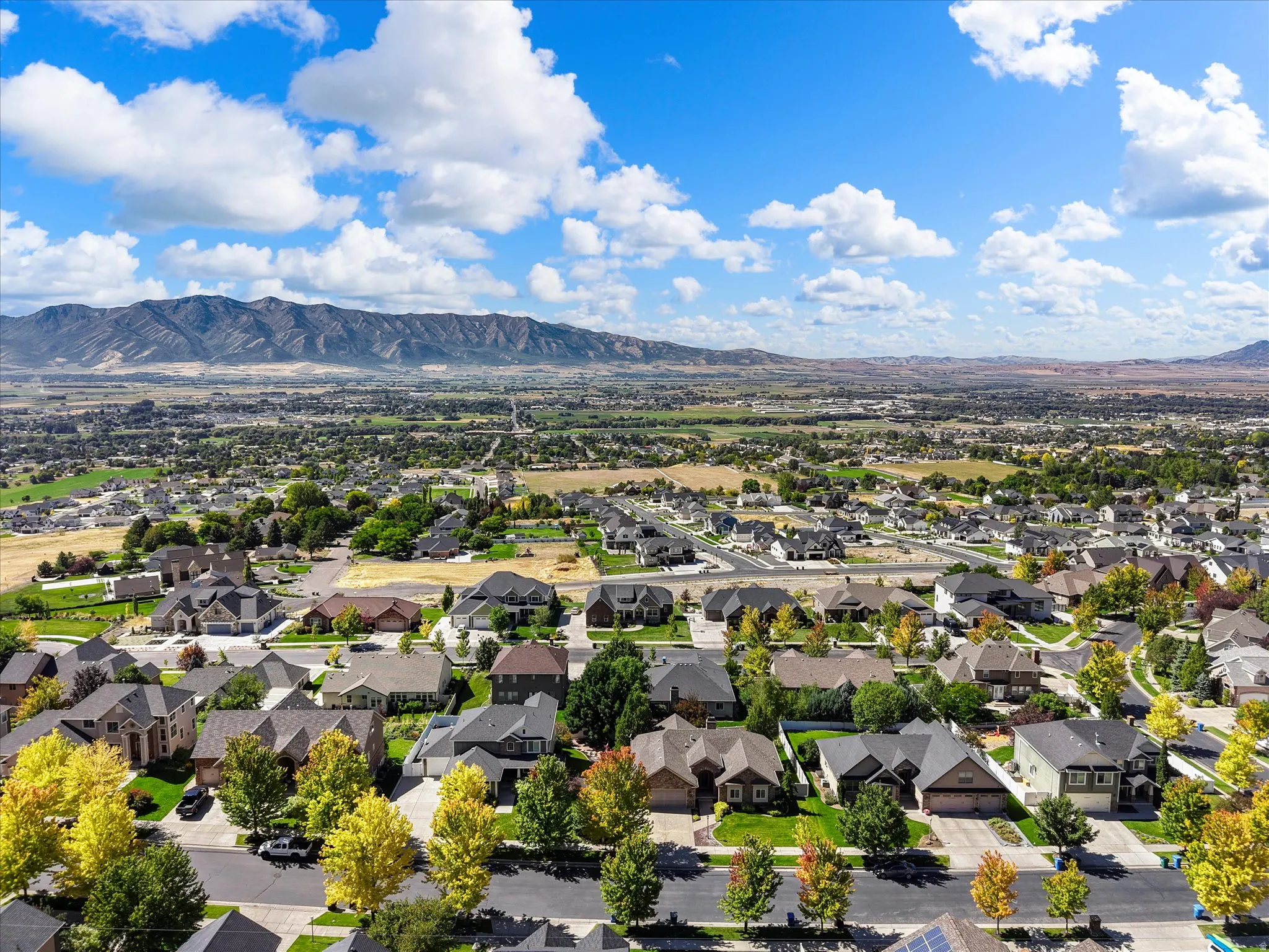 Aerial perspective of an established residential community nestled against mountain foothills, featuring tree-lined streets, spacious home sites with manicured landscaping, and expansive open space beyond the neighborhood perimeter