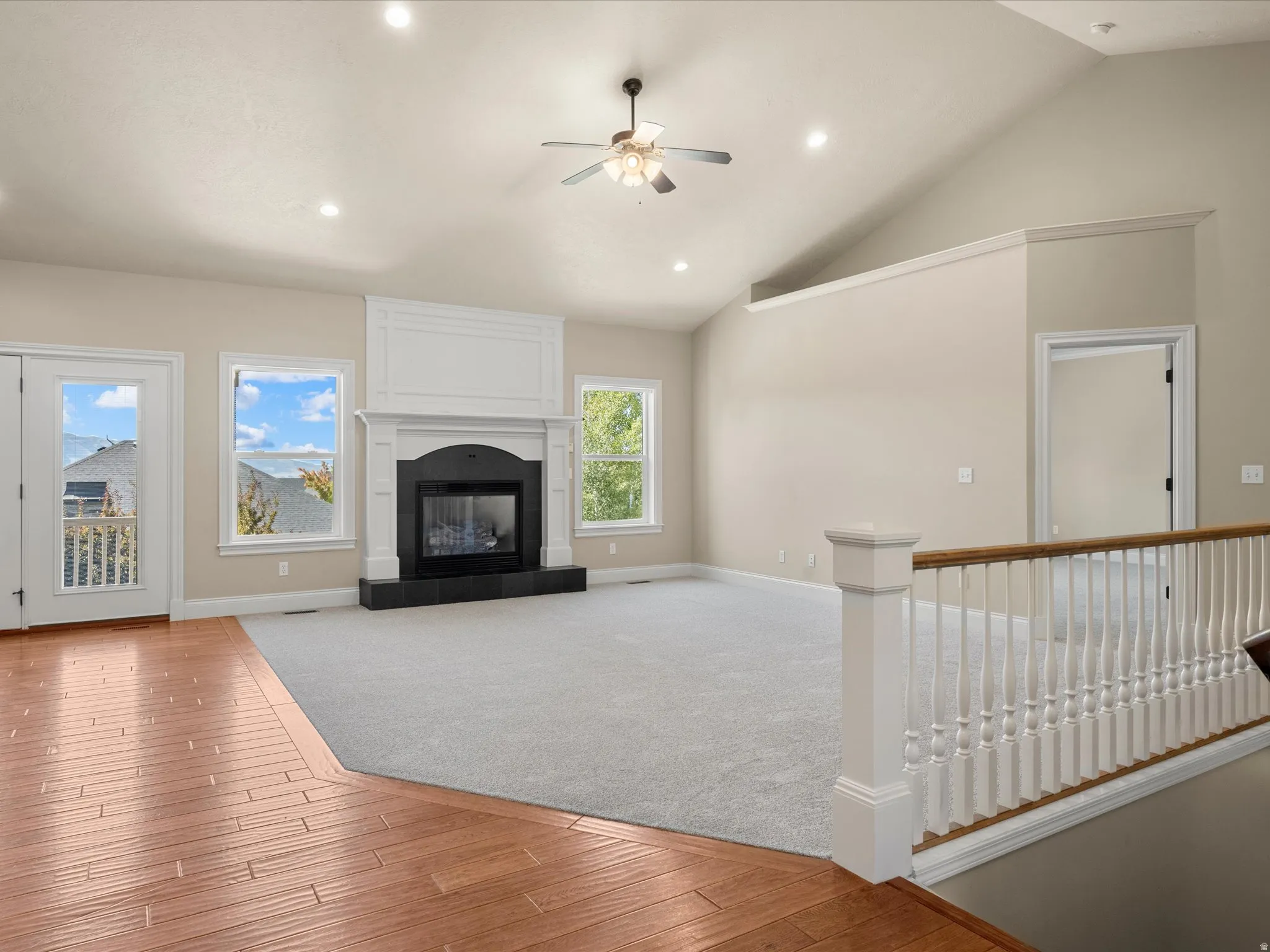 Vaulted ceiling with recessed lighting, fireplace with dark hearth, wood-finish flooring, and white spindle railing