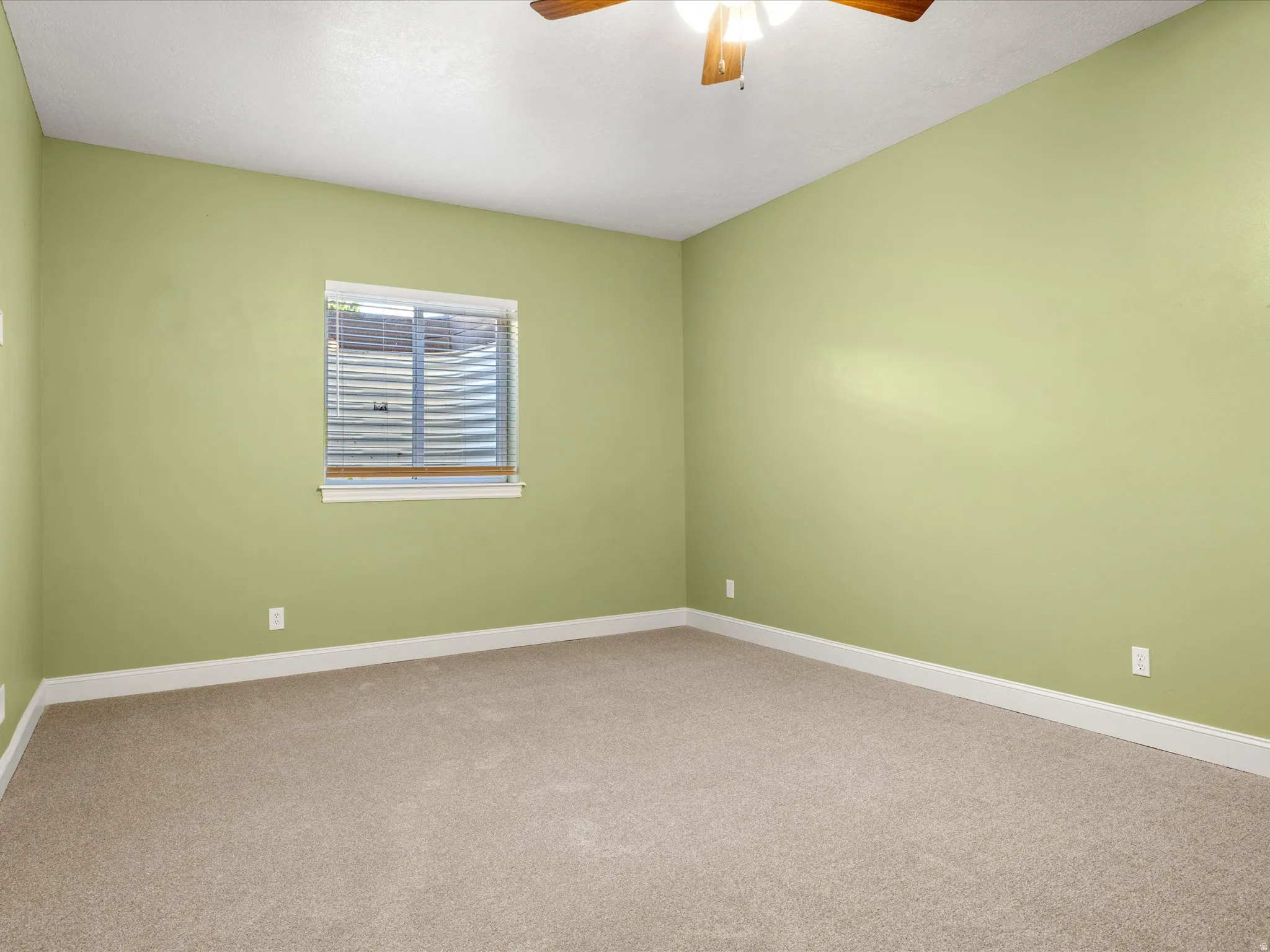 Neutral-toned carpet, light green wall paint, window with blinds, white window trim, and a ceiling fan