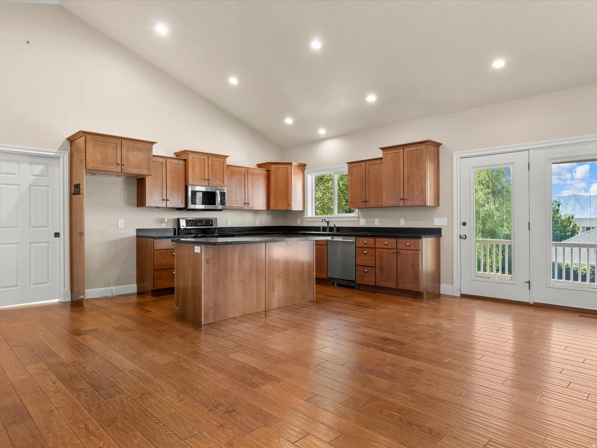 Cathedral ceiling with recessed lighting, wood-finish flooring, wood cabinetry, stainless steel appliances, and double patio doors