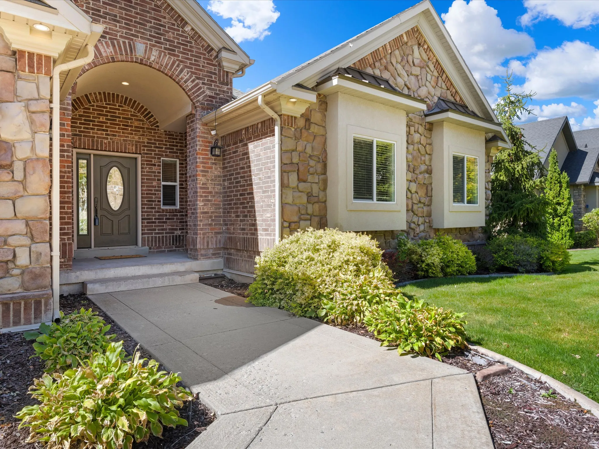 Brick and stone exterior with decorative bay windows, an arched entryway, and a concrete pathway