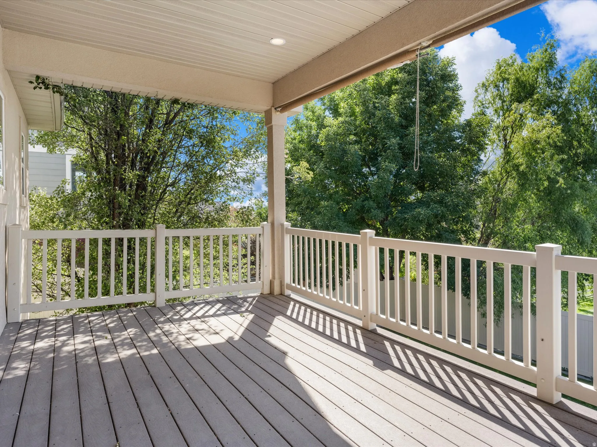 Covered outdoor deck with light-toned decking, white railings, and recessed ceiling lighting