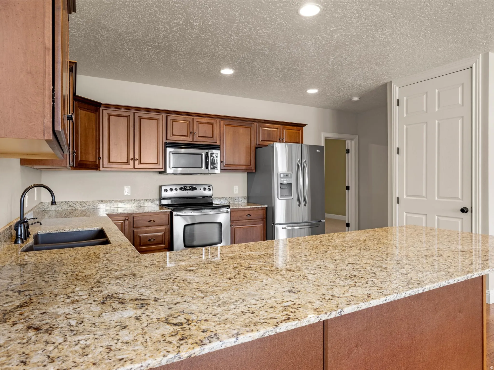 Kitchen featuring an expansive stone countertop, stainless steel appliances, dark wood cabinetry, and an undermount sink with a gooseneck faucet