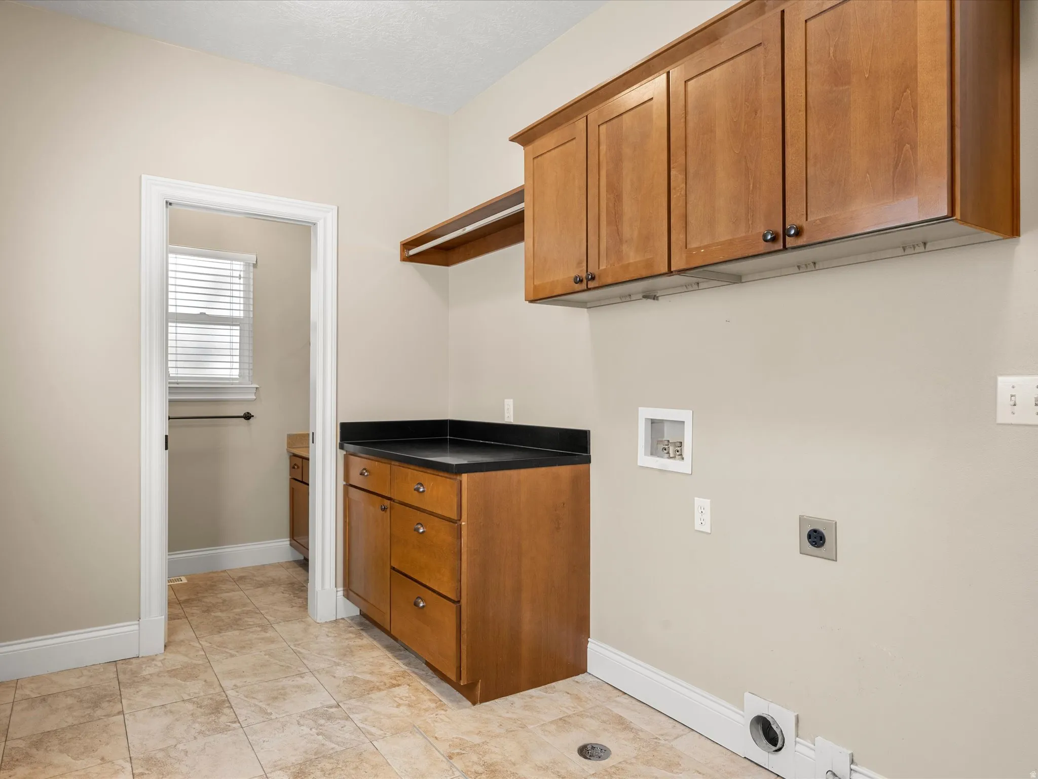 Upper and lower wood-finish cabinetry with dark countertops, tiled flooring, and neutral wall paint