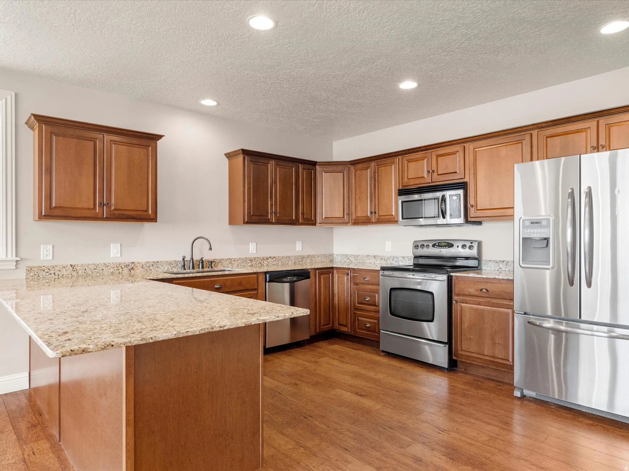Kitchen featuring wood-finish flooring, recessed lighting, wood cabinetry, granite countertops, and stainless steel appliances
