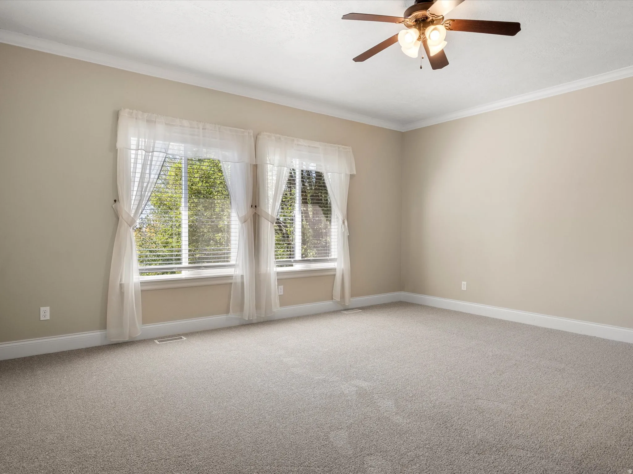 Expansive interior space featuring neutral tone walls, crown molding, and a ceiling fan with integrated lighting