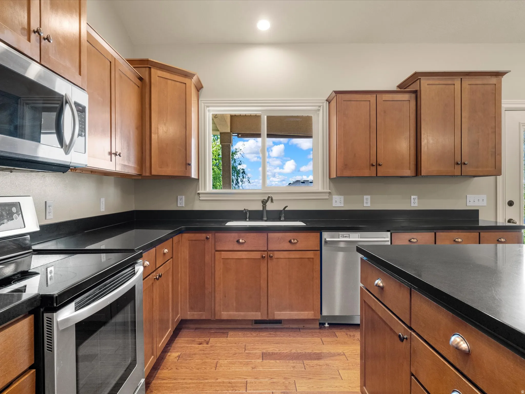 U-shaped kitchen featuring wood cabinetry, dark countertops, a stainless steel microwave, and a stainless steel dishwasher