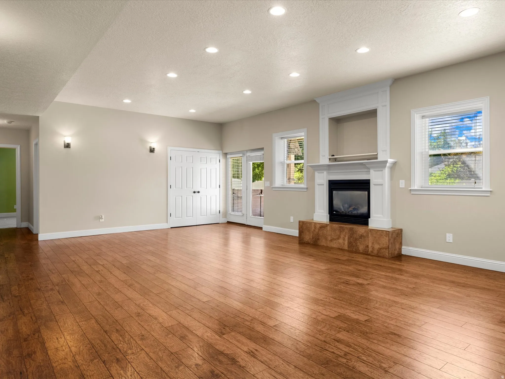 Spacious room featuring wood-finish flooring, recessed lighting, double doors, a fireplace with a white mantel, and two windows
