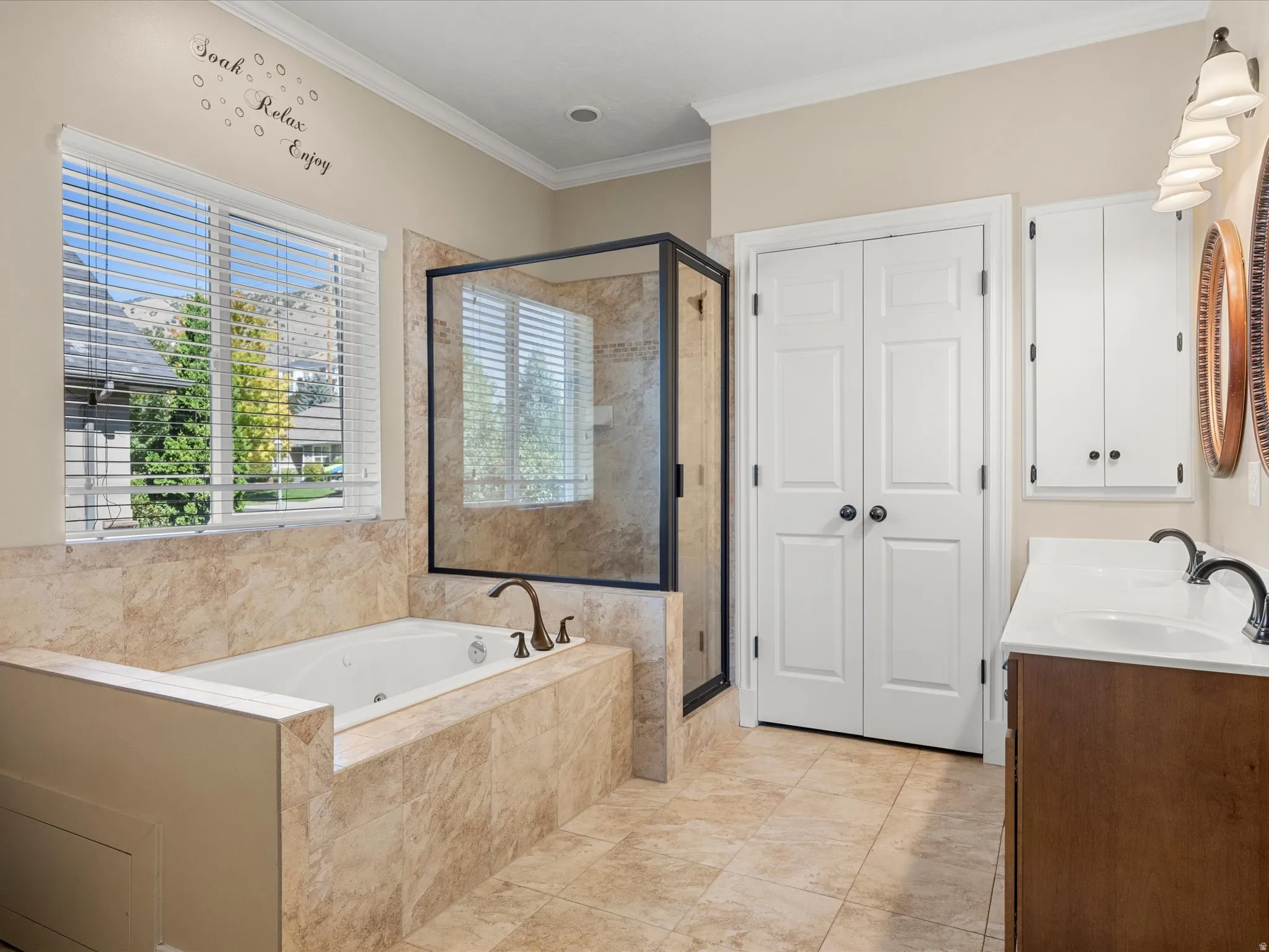 Soaking tub with a tiled surround, glass-enclosed shower, dual vanity with undermount sinks, and tile flooring