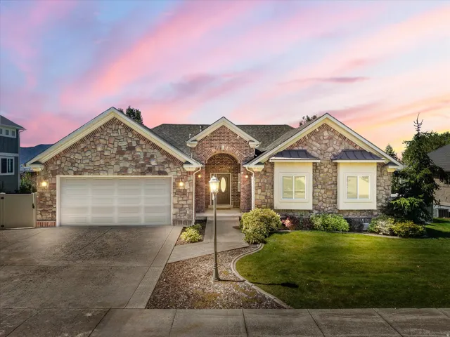 Stone and brick facade, arched entryway, attached garage, established landscaping, and a concrete driveway