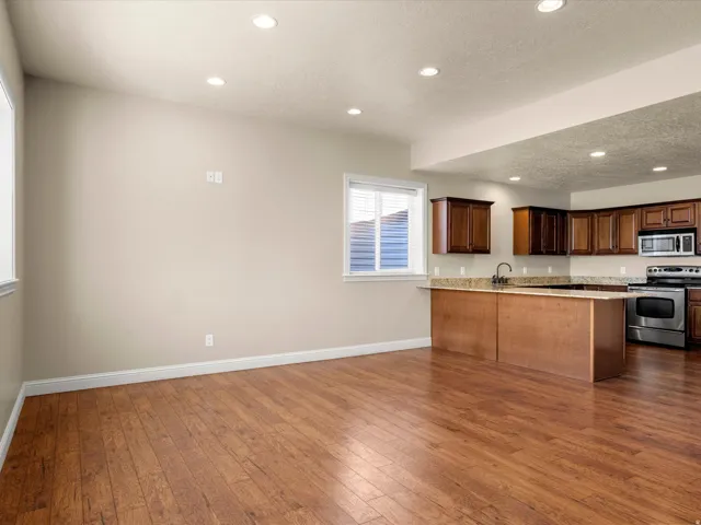 Wood-finish flooring, recessed lighting, and kitchen featuring wood cabinetry, stone countertops, and stainless steel appliances