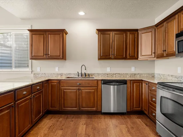 Kitchen featuring wood-finish flooring, L-shaped cabinetry, light-toned countertops, a stainless steel sink with a gooseneck faucet, and stainless steel appliances