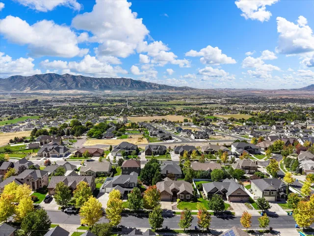 Aerial perspective of an established residential community nestled against mountain foothills, featuring tree-lined streets, spacious home sites with manicured landscaping, and expansive open space beyond the neighborhood perimeter
