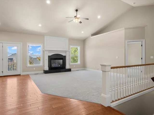 Vaulted ceiling with recessed lighting, fireplace with dark hearth, wood-finish flooring, and white spindle railing
