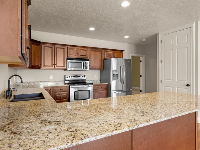 Kitchen featuring an expansive stone countertop, stainless steel appliances, dark wood cabinetry, and an undermount sink with a gooseneck faucet