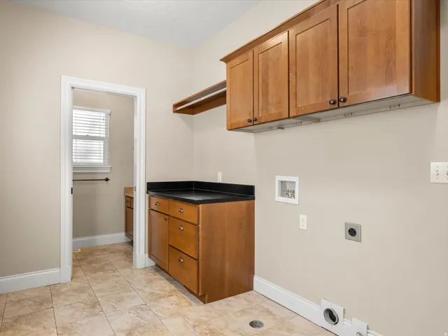 Upper and lower wood-finish cabinetry with dark countertops, tiled flooring, and neutral wall paint