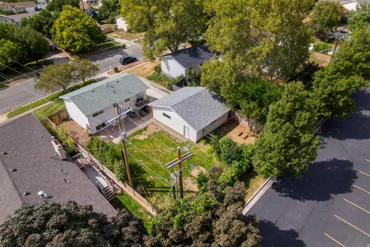 Aerial view of a contemporary home situated on a landscaped lot with mature trees, fenced perimeter, and a two-car driveway