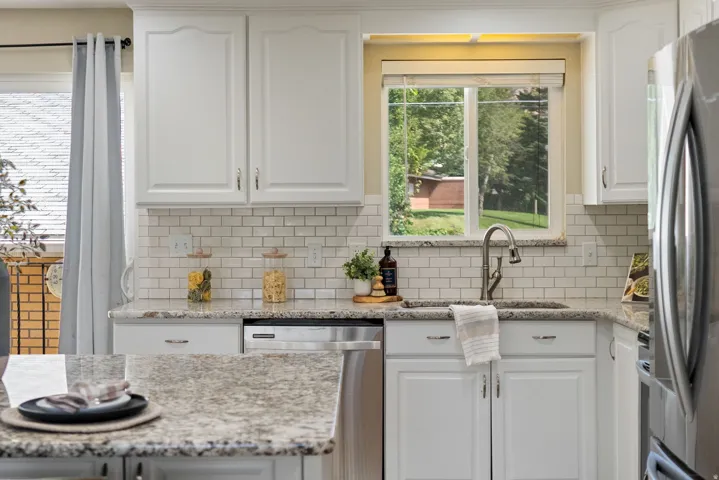 White cabinetry with brushed nickel hardware, granite countertops, subway tile backsplash, stainless steel appliances, and a stainless steel sink with a gooseneck faucet