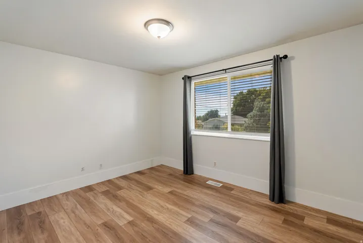 Wood-finish flooring, white walls, flush mount ceiling light, and a window with blinds