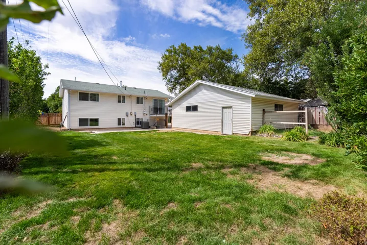 Expansive lawn with a detached auxiliary building, concrete patio, and upper-level balcony