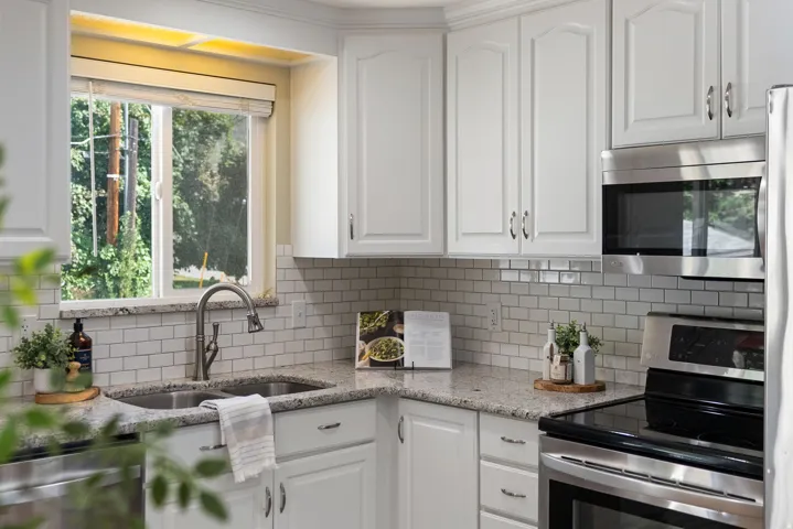 White shaker-style cabinetry with stainless steel hardware, granite countertops, subway tile backsplash, and stainless steel appliances