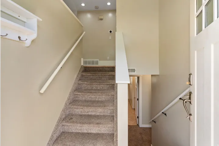 Carpeted staircase with white handrails and recessed lighting