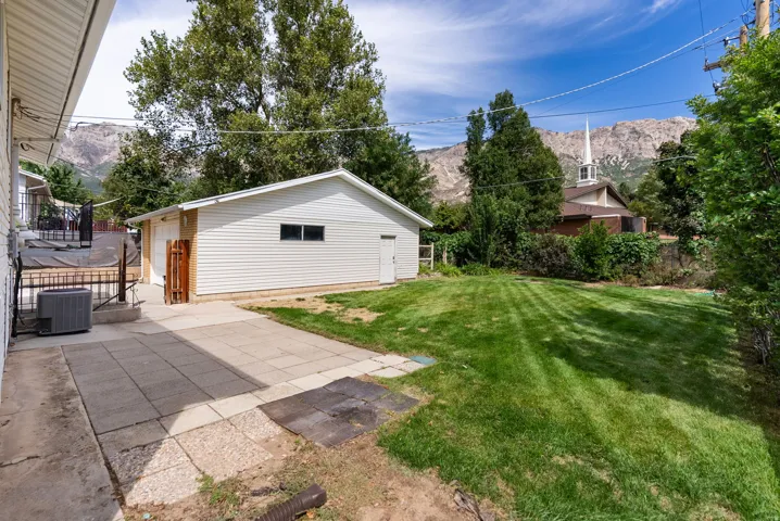 Expansive lawn with mountain backdrop, detached garage, and paved patio