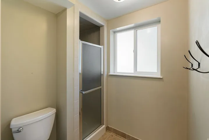 Shower stall with frosted glass door, white window with frosted pane, and light-toned tile flooring