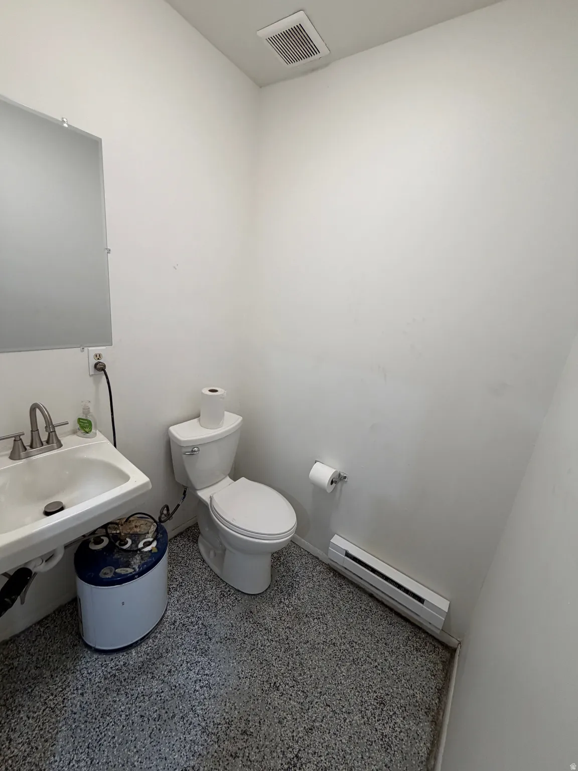 Powder room with a white wall-mounted sink, toilet, wall-mounted mirror, and speckled flooring