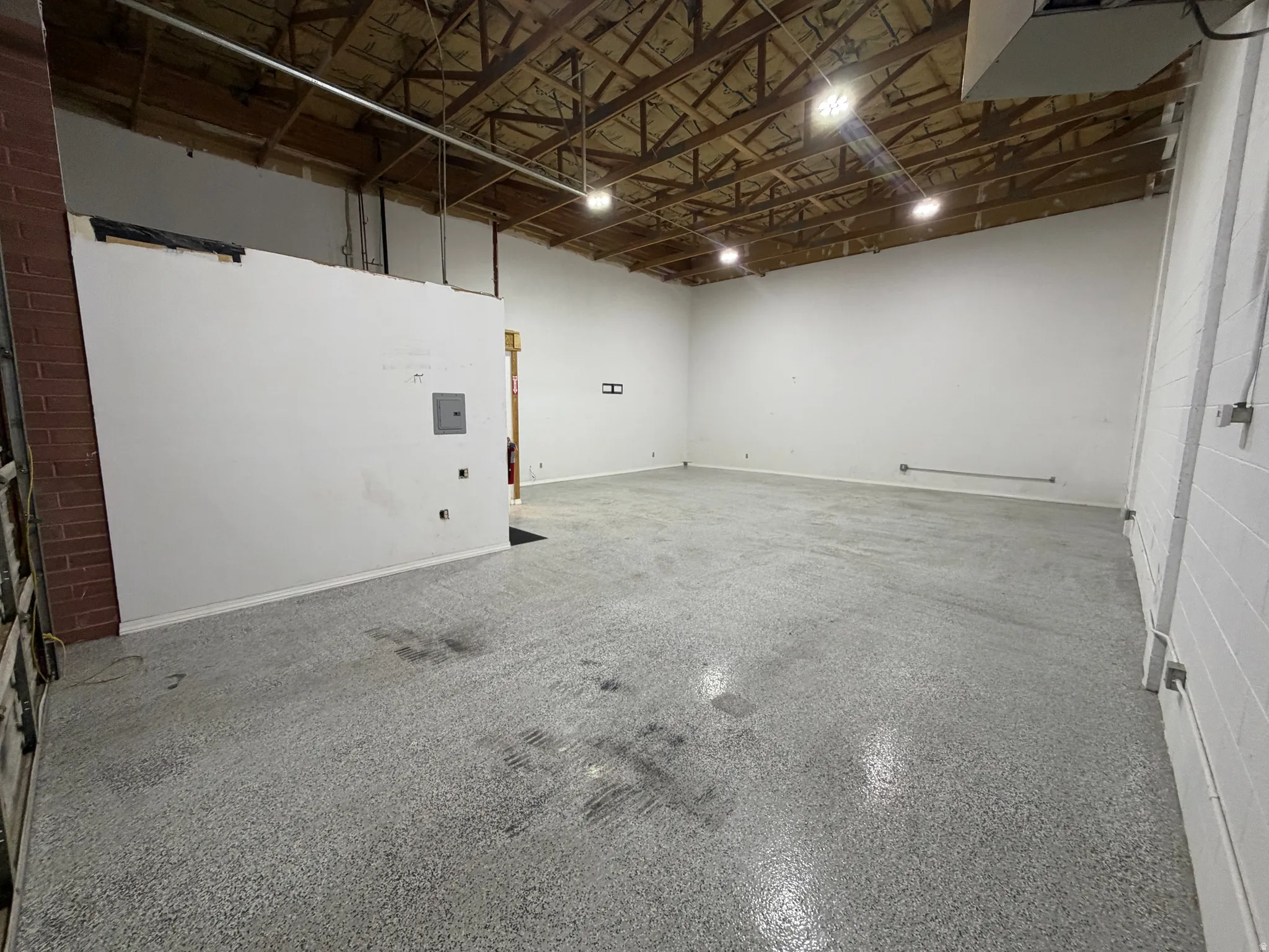 Exposed wood beam ceiling, recessed lighting, polished concrete flooring, white painted walls, and an electrical panel