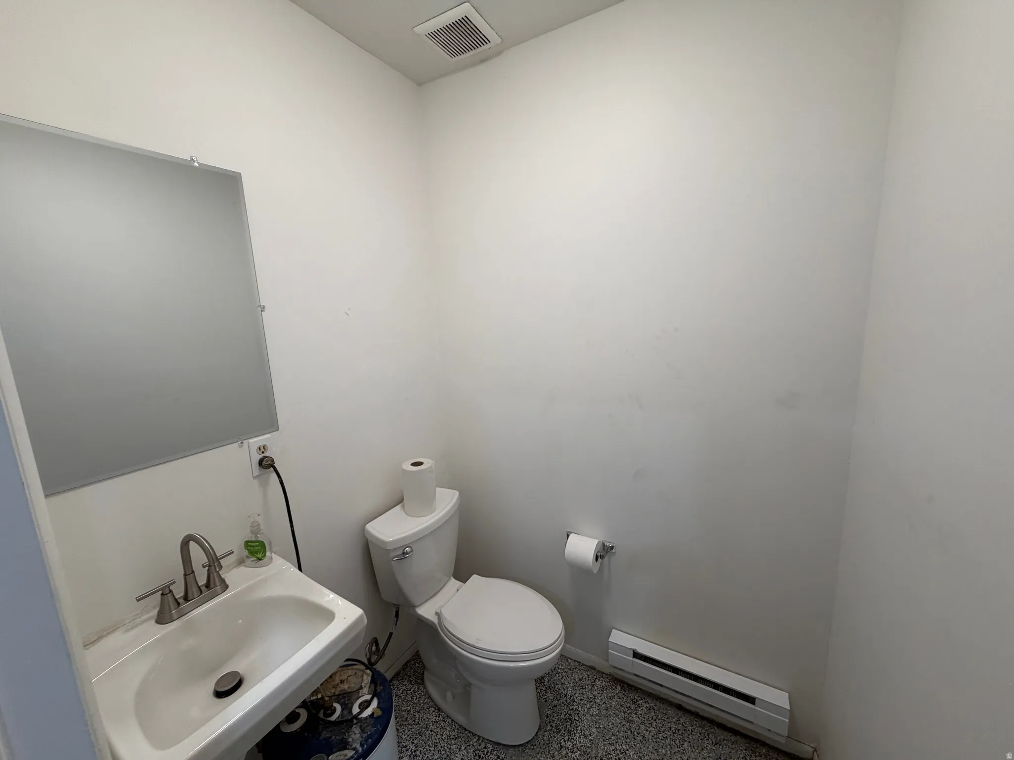 Recessed lighting fixture, wall-mounted mirror, ceramic sink, brushed nickel faucet, and speckled flooring