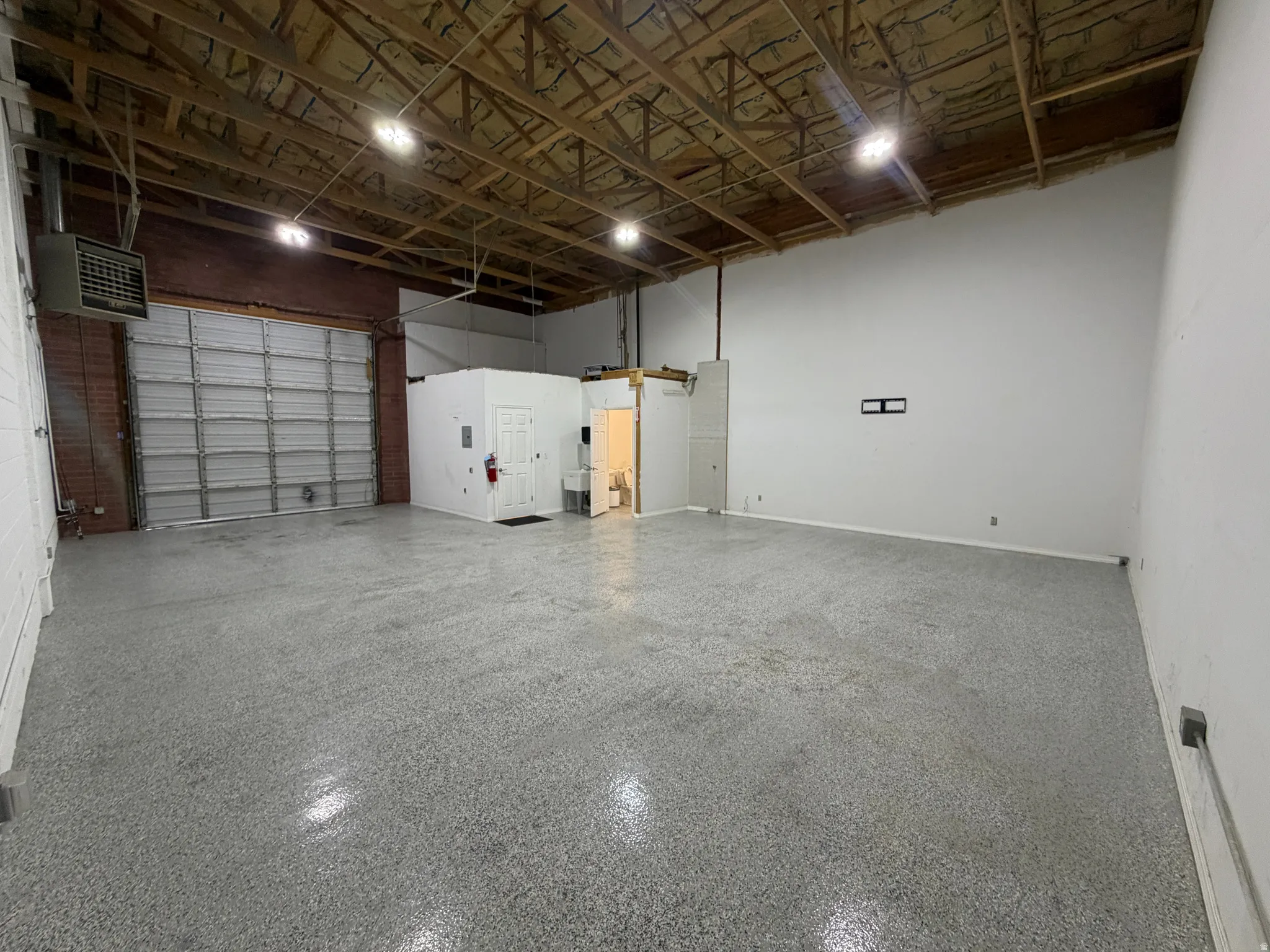 Spacious open concept interior with exposed wood beam ceiling, large roll-up door, and polished concrete flooring