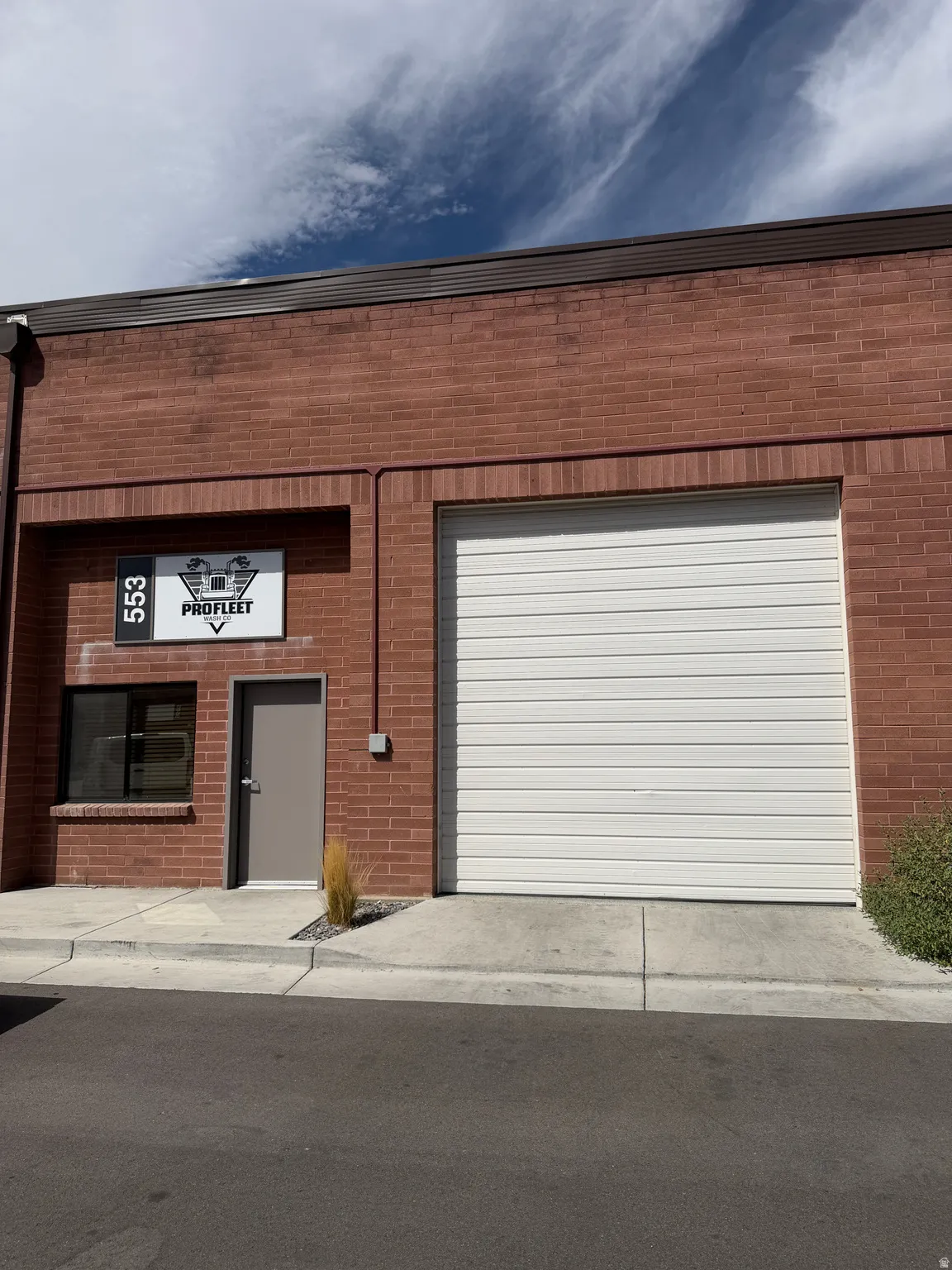 Red brick exterior with a large white roll-up door, a separate pedestrian entry, and an exterior window