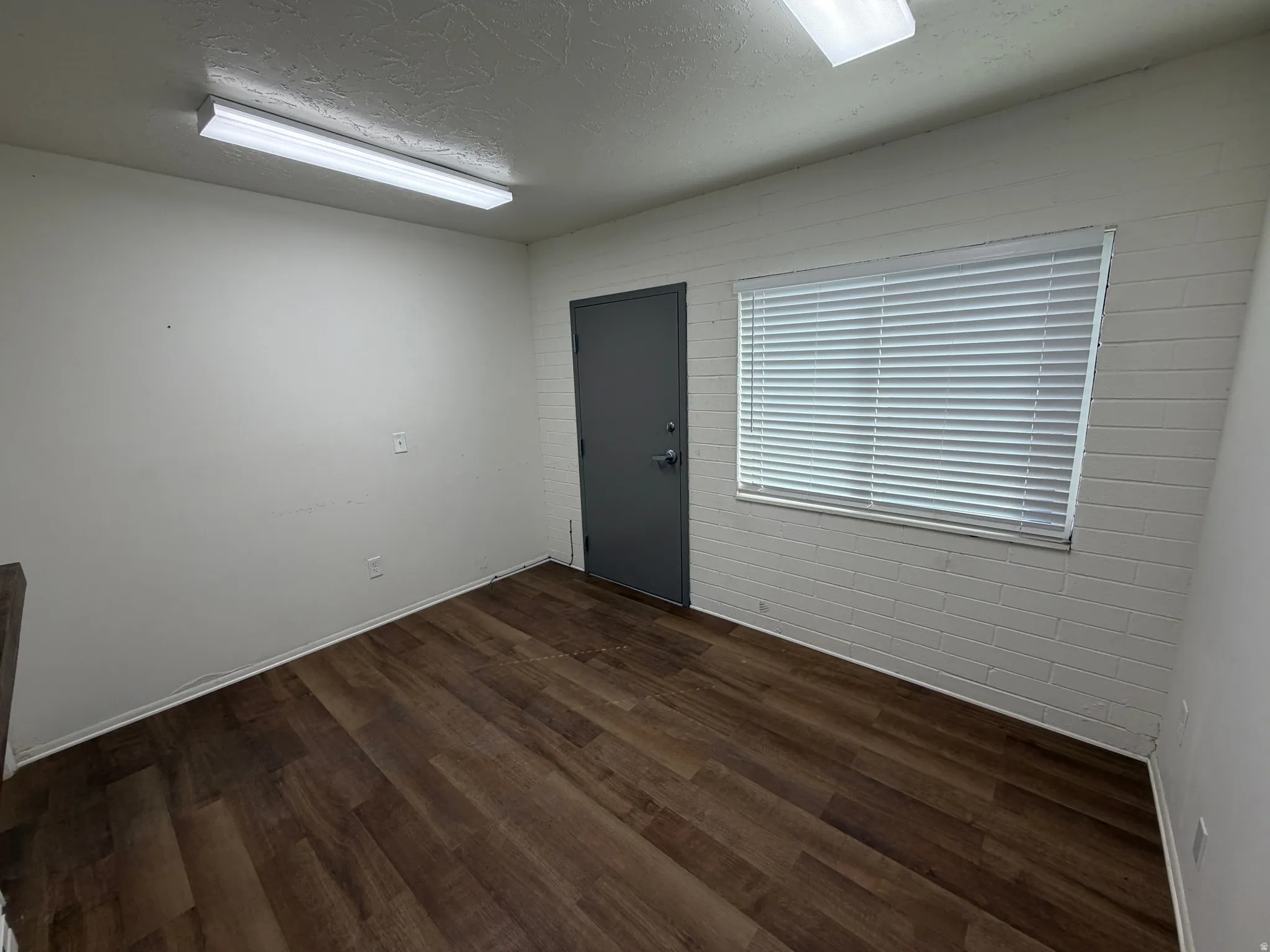 Wood-finish flooring, white walls, white brick accent wall, window with blinds, and flush-mounted ceiling light fixtures