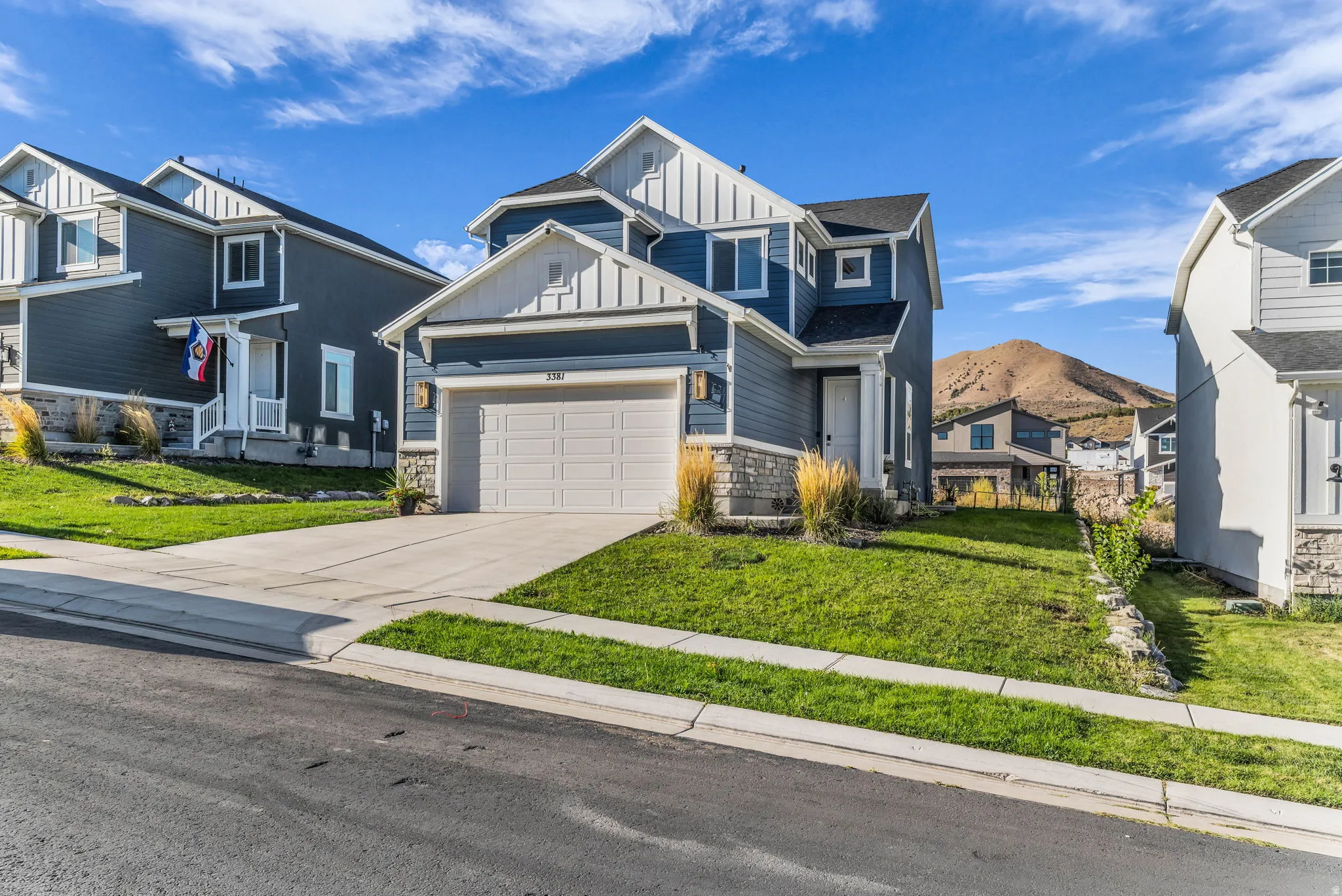 Two-story residence featuring blue siding, white trim, stone accents, an attached garage, and a concrete driveway