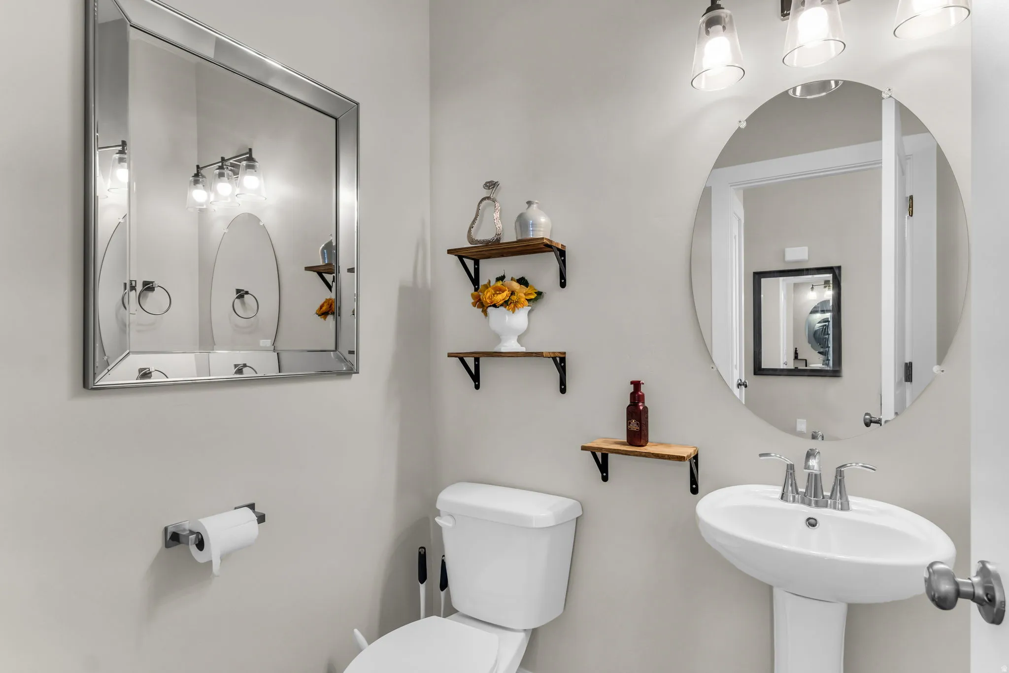 Pedestal sink with chrome faucet, wall-mounted light fixture, and square mirror with a beveled frame
