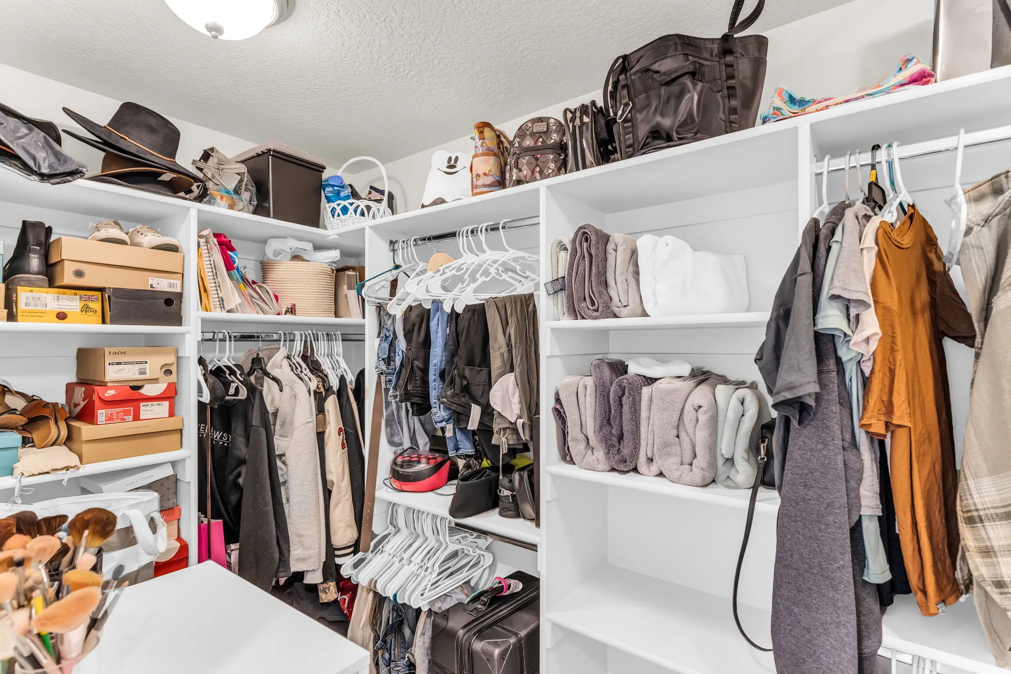 Walk-in closet featuring white built-in shelving, multiple hanging rods, and recessed lighting