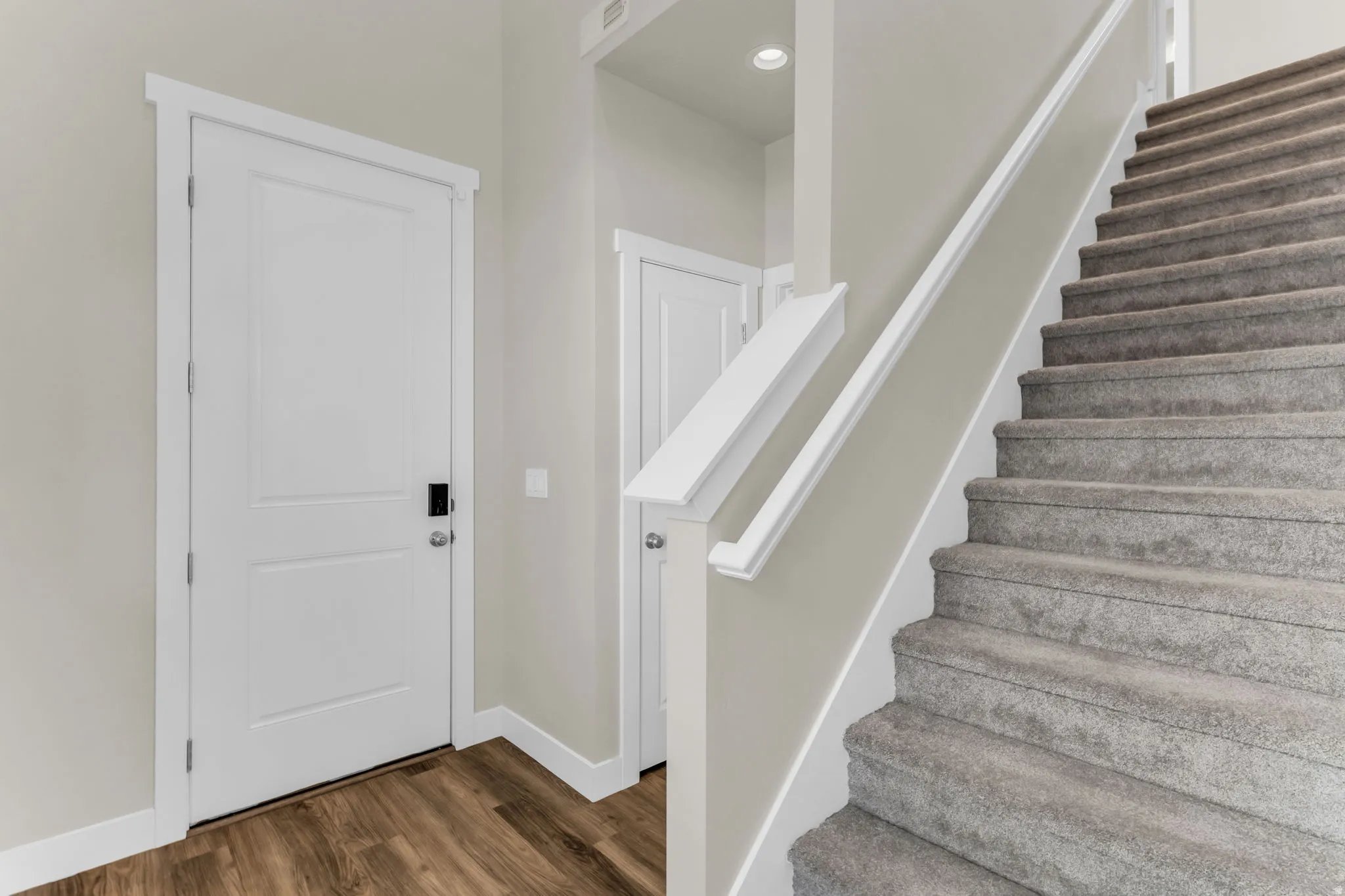 Wood-finish flooring, white paneled doors, carpeted staircase, white railing, recessed lighting